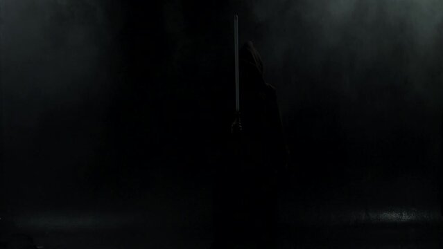Young man in Jedi cosplay costume with lightsaber battle on black background in smoke and rain, 4k slow motion video filmed on 8k camera nikon z9