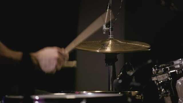 A young Caucasian man drummer plays a drum kit in a music studio. Creates music and art. Drum set, drum kit in dark, drummer plays. The rock band is rehearsing, studying. The musician is playing