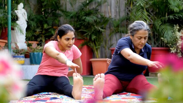 A middle-aged woman and her daughter doing toe-touching exercises on a Yoga mat - home workout. Two females doing Yoga in the morning - healthy lifestyle  fitness regime  yoga trainer  old age prob...