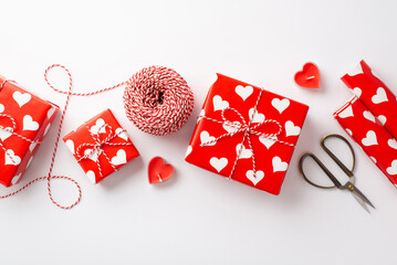 Valentine's Day concept. Top view photo of gift boxes wrapping paper rolls heart shaped candles spool of twine and scissors on isolated white background