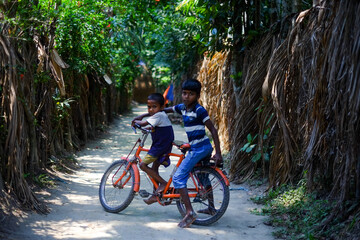 Bangladeshi rural kid is learning how to ride a bicycle on a village road with his elder brother who is also a kid