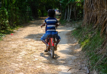 Bangladeshi rural kid is learning how to ride a bicycle on a village road with his elder brother who is also a kid