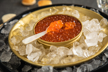 Orange Keta Lachs Kaviar in Dose auf Eis in Glas Schale mit Perlmutt Löffel, Sekt Champagner und Toast Brot auf dunkel Serviette und schwarz Schiefer