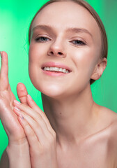 Obraz na płótnie Canvas Beauty and skin care. Happy woman with fresh radiant, moisturized skin, standing with bare shoulders, with light makeup and natural skin on a green background. 