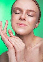 Obraz na płótnie Canvas Beauty and skin care. Happy woman with fresh radiant, moisturized skin, standing with bare shoulders, with light makeup and natural skin on a green background. 