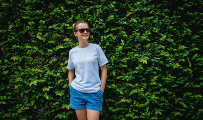 Fototapeta premium Female model wearing white blank t-shirt on the background of an leafes wall.