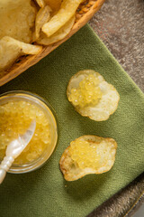 Gelber Saiblings Kaviar mit Perlmutt Löffel zu Kartoffelchips Chips in Korb als Gourmet Snack auf Serviette grün, Silber Teller und Marmor hell