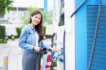 Unrecognizable Asian woman holding the CCS 2 EV charging connector at EV charging station, woman...