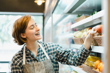 Happy cheerful caucasian grocery store staff arranging a vegetables and fruits on the shelf.