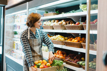 Happy cheerful caucasian grocery store staff arranging a vegetables and fruits on the shelf. 