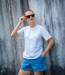 Female model wearing white blank t-shirt on the background of an gray scratched wall.