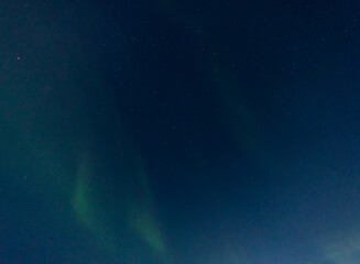 Green and purple northern lights in iceland with the sky bluish by the moon