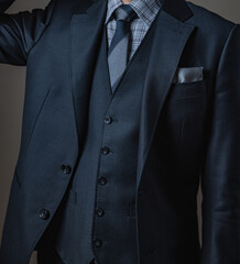 Smart young man in three-piece luxury black suit on gray background.