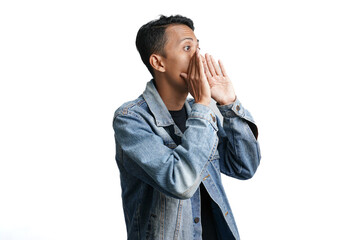 asian man wearing blue jean jacket shouting giving information with hand near mouth, isolated on...