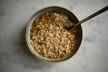 round plate with prepared instant noodles and black spoon close-up top view. ready ramen noodles. cooked ramen broth