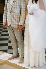 The bride and groom hold hands and stand on embroidered towel, traditionally at a wedding ceremony in the church. View of the feet of the newlyweds. Bottom view.