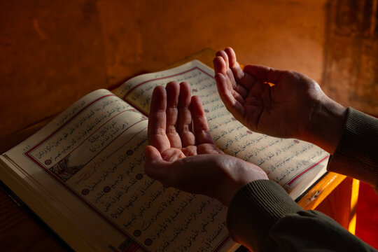 Muslim woman praying in a mosque with raising hands and Holy Quran on background