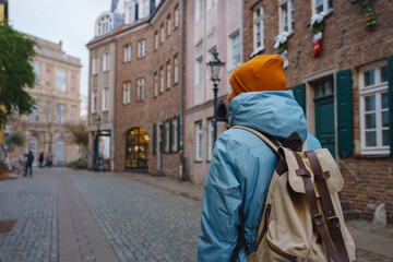 winter travel to Dusseldorf, Germany. young Asian tourist in blue jacket and yellow hat (symbol of Ukraine) walks through sights of old town or Altstadt. Popular center of Rheinland and Westphalia - obrazy, fototapety, plakaty
