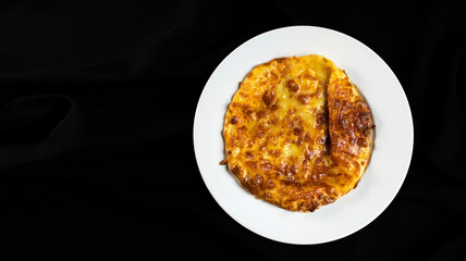 Top view of baked khachapuri on white plate on black background, traditional georgian dish with cheese