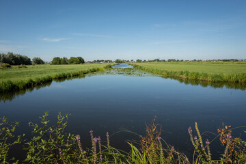 Typical Dutch rural scenery showing the flat Netherlands. canal water is part of a flood management system for the polder which is land reclaimed from the sea and converted into arable farm fields