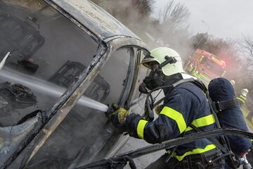 Firefighter with a breathing apparatus mask extinguishes a car fire using water