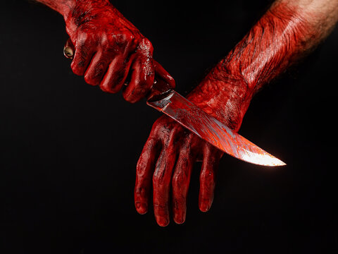 A man wipes a bloody knife with his hand on a black background. 