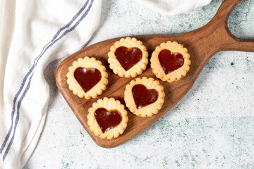 Fototapeta na wymiar Heart shaped cookies on wooden serving board on gray background. Cookies with marmalade filling in the middle. Bakery desserts. Top view
