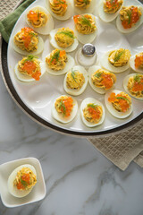 Gefüllte teuflische russische Eier mit Dill und orange Keta Lachs und gelb Saibling Kaviar auf Eierteller, Serviette grün, Silber Teller und Marmor Hintergrund hell