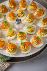 Gefüllte teuflische russische Eier mit Dill und orange Keta Lachs und gelb Saibling Kaviar auf Eierteller, Serviette grün, Silber Teller und Marmor Hintergrund hell