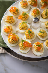 Gefüllte teuflische russische Eier mit Dill und orange Keta Lachs und gelb Saibling Kaviar auf Eierteller, Serviette grün, Silber Teller und Marmor Hintergrund hell