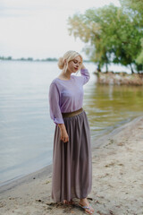 Blonde girl on a summer day on the shore near the river in nature in a dress