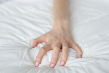 Strongly clenched female hand on sheet on bed