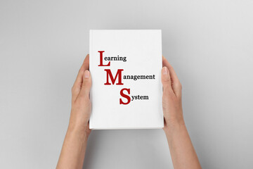 Woman holding book with text Learning Management System and red initial letters forming initialism...