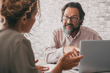 Back view of woman and man in office. Consultant and client sitting at the desk talking and using laptop. Professional at work. Business and office lifestyle concept. Modern people and computer