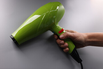 Woman hands hold a green hair dryer on gray background