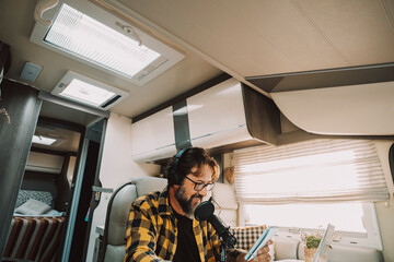 One modern traveler young adult man speaking at the microphone in podcast recording business activity. Digital nomad and smart working inside a camper van. People at work in alternative office desk