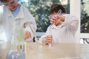Selective focus on a little girl's hands, pouring reagent from a test tube into other test tube with chemicals, during chemistry class, in the school laboratory. School, education and learning concept