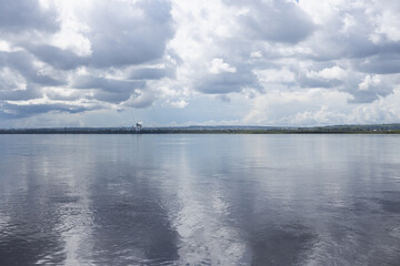 Blue deep river landscape with white fluffy clouds in sunlights with beautiful reflection on water mirror surface and thin line of horizon. Tranquil and relax minimalistic landscape in grey color.