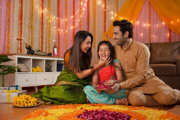 Fototapeta na wymiar Stock image of a happy family - mother loving her daughter. Making rangoli and enjoying Diwali. Indian mother and father loving their daughter and sitting together to make rangoli - home decoration...