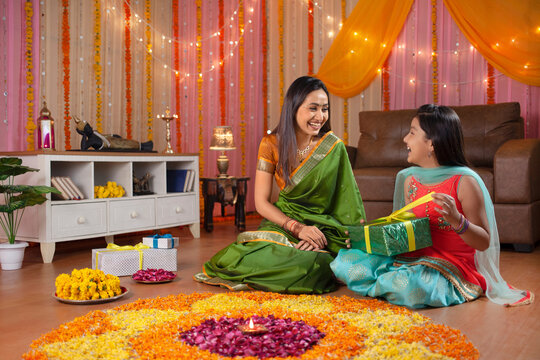 Indian mother presenting her daughter with surprise gift on Diwali festival. Stock image of a mother surprising her daughter on Diwali festival night with a gift  little girl helping her mother in ...