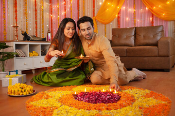 Diwali Celebration - Indian wife holding tray / thali of diyas and husband arranging diyas to decorate home. Stock image of an Indian couple holding tray / thali of diyas and arranging diyas on ran...