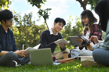 Asian college students talking and working on group project while sitting on on campus lawn on beautiful day