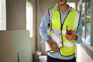 Engineer man wearing yellow vests holding clipboard and walkie talkie standing in construction site