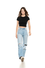 Young female model wearing ripped jeans and black shirt walking on a white background. Front view