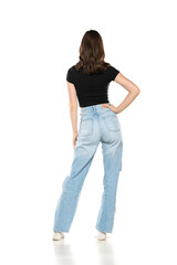 Young female model wearing jeans and black shirt posing on a white studio background. Back, rear view