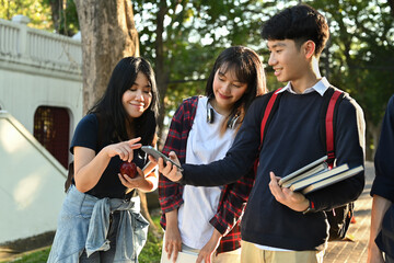 Group of asian students using mobile phone while walking together outdoors at university campus. Youth and community concept