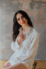 Fototapeta premium Sexy young brunette girl in a white shirt and lingerie in a loft photo studio