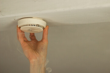 Male hand changing the battery and fixing the smoke alarm on ceiling of a home. Home or office...