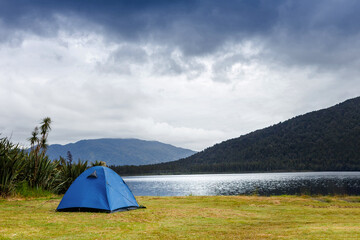 Obraz premium Camping and tent under the rainy forest near the lake with beautiful mountains background