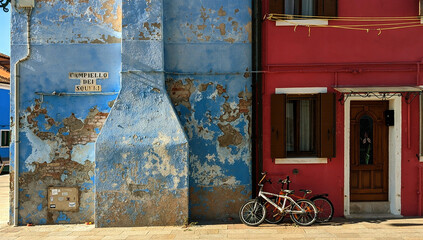 un vélo posé sur le mur décrépis d'une maison bleue et rouge